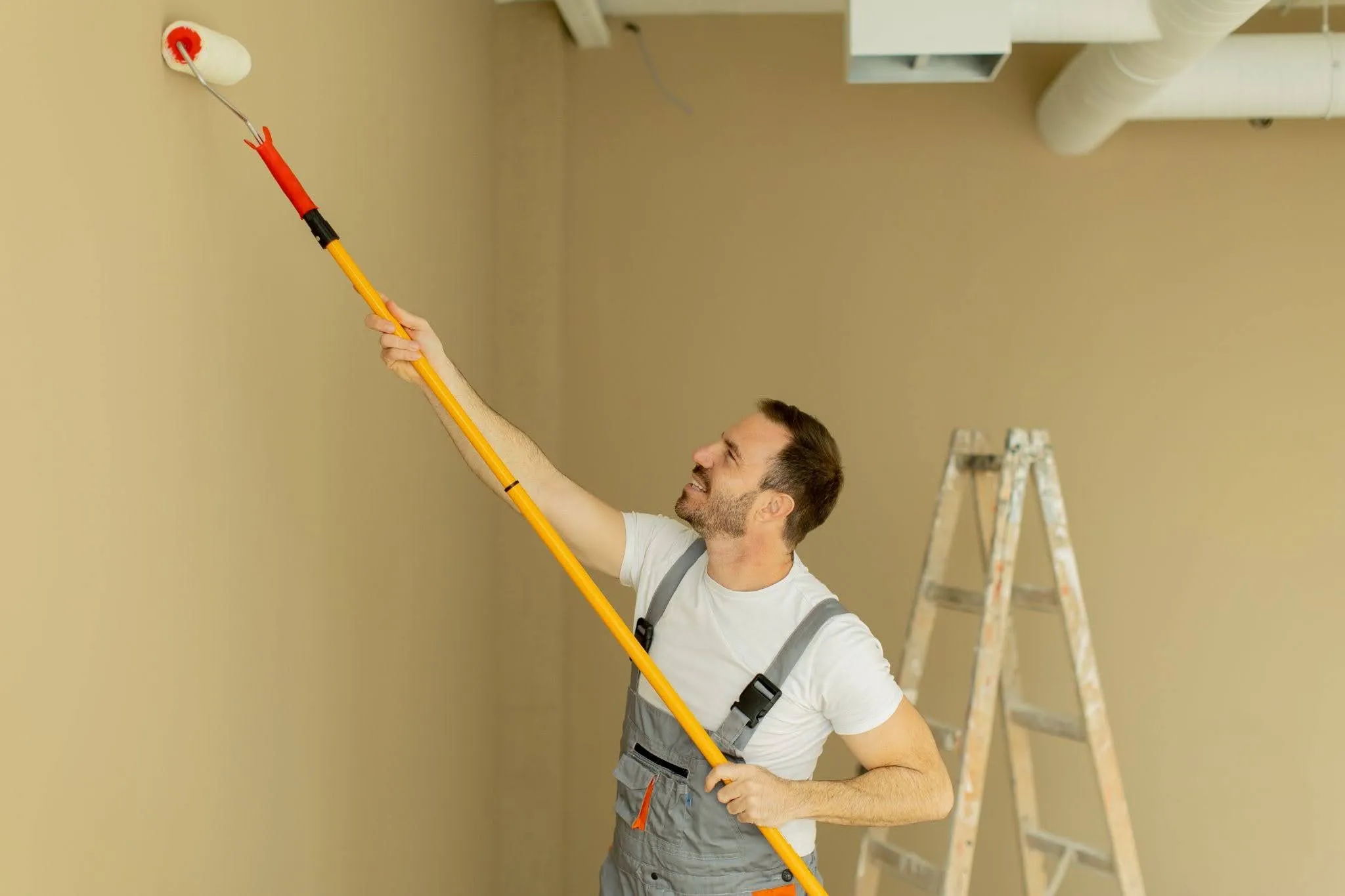 high-value-interior-painting-roller Painter using an extension roller for high-value interior painting projects in a large room with a ladder
